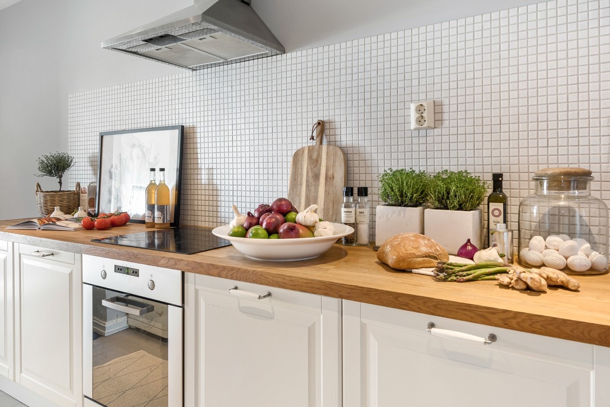 Det er lagt hvite mosaikkfliser på veggen, og av hvitevarer er det integrert stekeovn og keramisk topp. Forøvrig er det vegghengt kullfilterventilator, opplegg for oppvaskmaskin og avsatt plass til kjøl/frys på den ene enden. Galleribilde