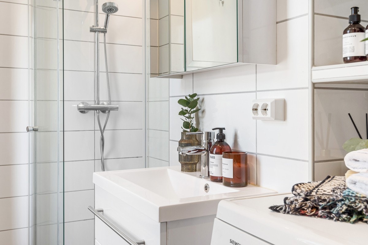 Videre er det speilskap, heldekkende servant på hvitt skuffemøblement, matchende høyskap og tre flislagte hyller i vaskesonen hvor det er opplegg for vaskemaskin. Galleribilde