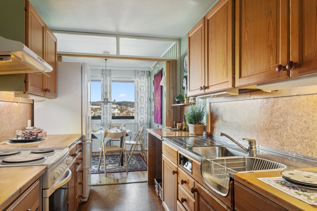 Kjøkkeninnredning med profilerte fronter. Heltre benkeplate, beslag med utslagsvask og oppvaskkum og 1-greps blandebatteri. Ventilator med kullfilter, korkfliser over benkeplate samt lys under overskap. Galleribilde