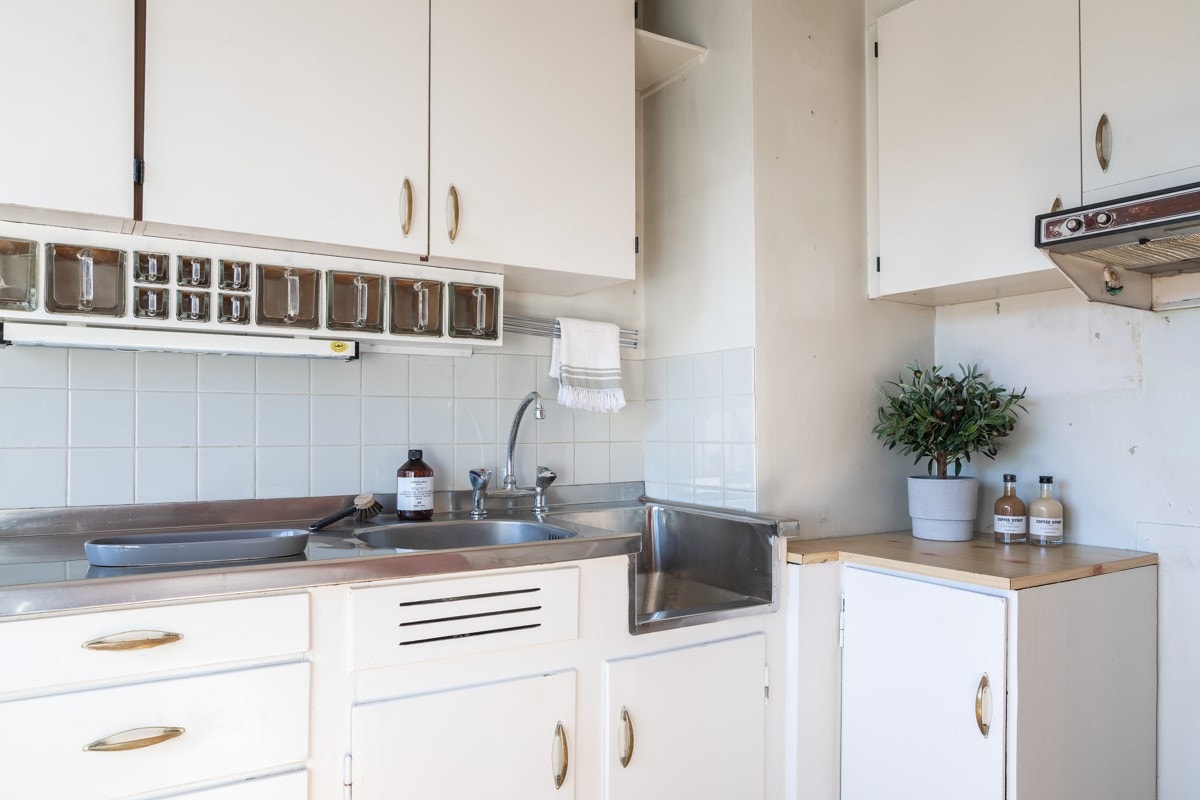 Kjøkkeninnredningen har malte slette fronter, overskap med benkebelysning og fliser på vegg. Videre er det integrert avtrekksvifte, samt opplegg for oppvaskmaskin og komfyr. Galleribilde