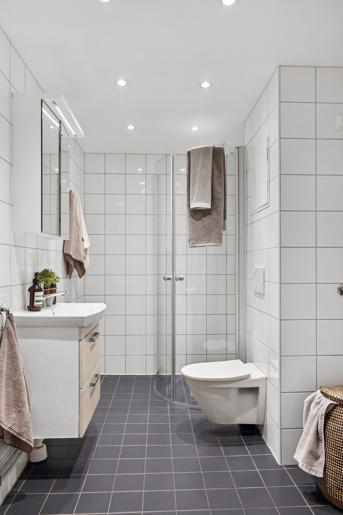 Baderomsinnredningen består av servantskap med helstøpt servant, speilskap, vegghengt toalett og dusjhjørne med buende svingdører av herdet glass, sluk av plastmateriale med klemring og synlig membran. Galleribilde