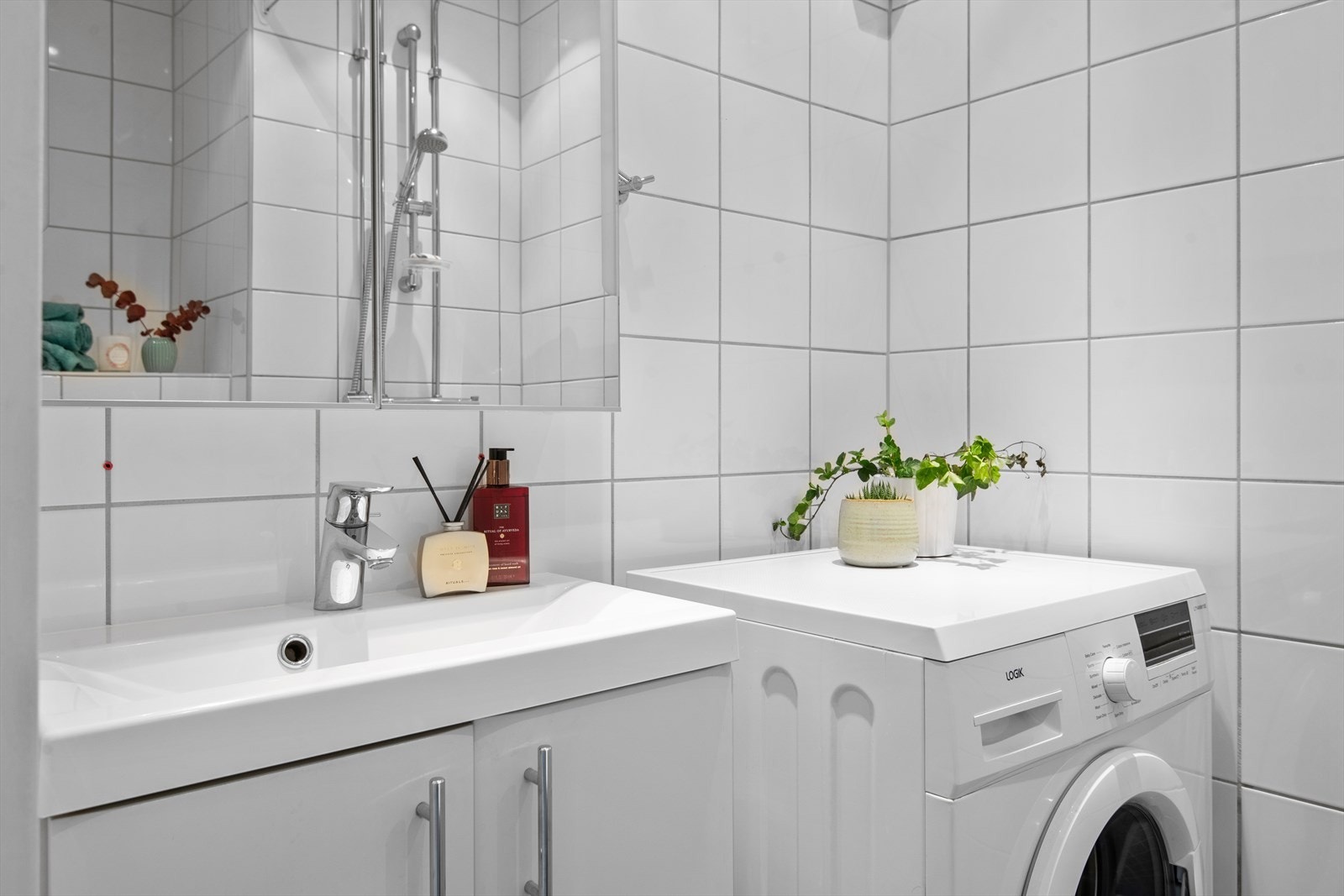 Badet er innredet med vegghengt toalett med innebygget sisterne, baderomsmøbel med servant, speilskap med lysarmatur, skjermet dusjhjørne med dusjforheng, blandebatteri og dusjgarnityr. Galleribilde