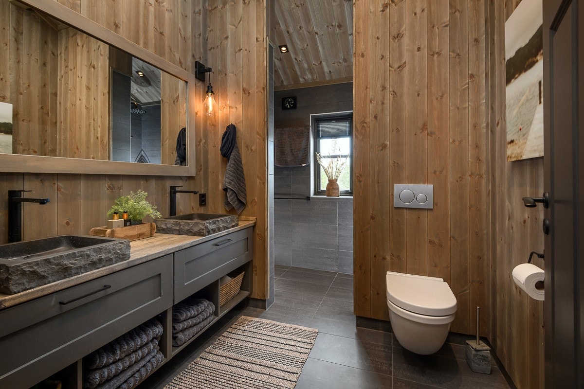 Badet er lekkert med mørke gulvfliser og beisede panelvegger Galleribilde
