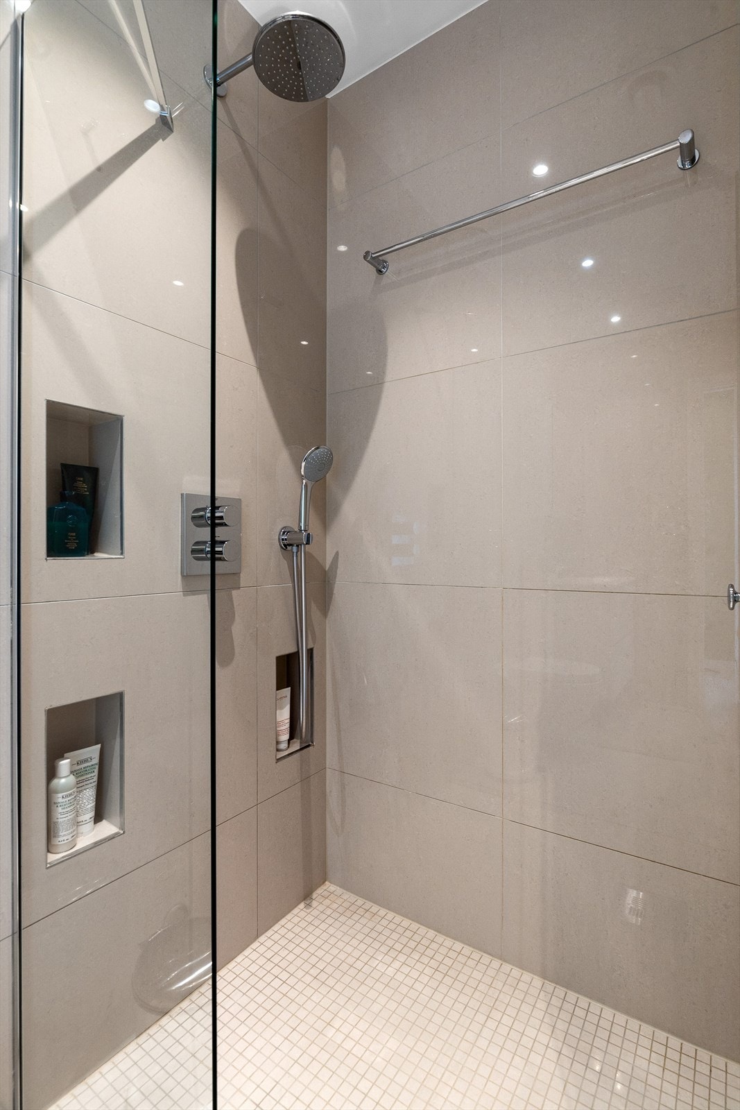 Badet inneholder vegghengt innredning med heldekkende servant, overskap med speildører, dusjnisje med glassdør og regnfallsdusj og vegghengt toalett Galleribilde