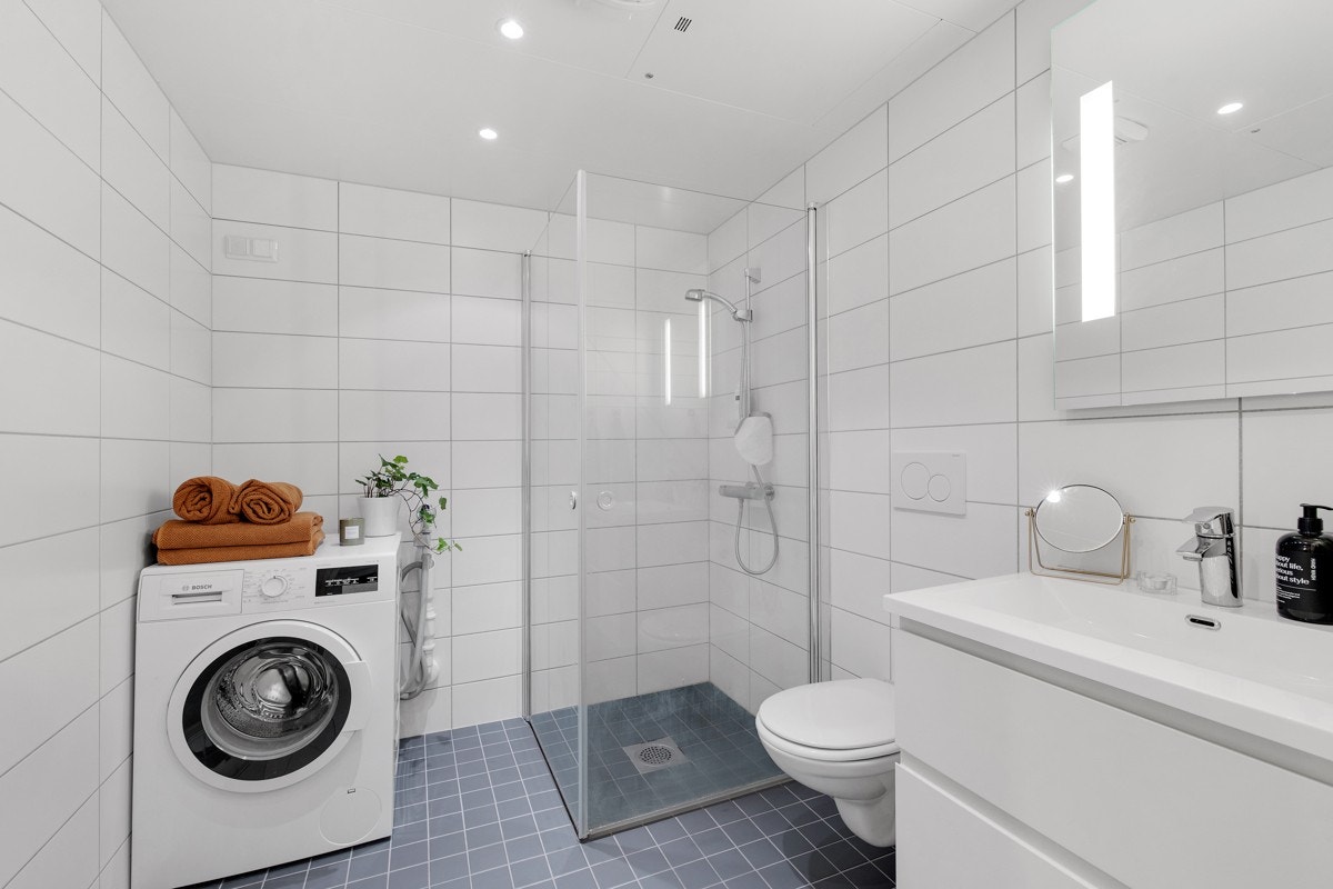 Baderommet har mørke fliser på gulv med gulvvarme, lyse fliser på veggene og downlights i himlingen. Opplegg for vaskemaskin. Galleribilde