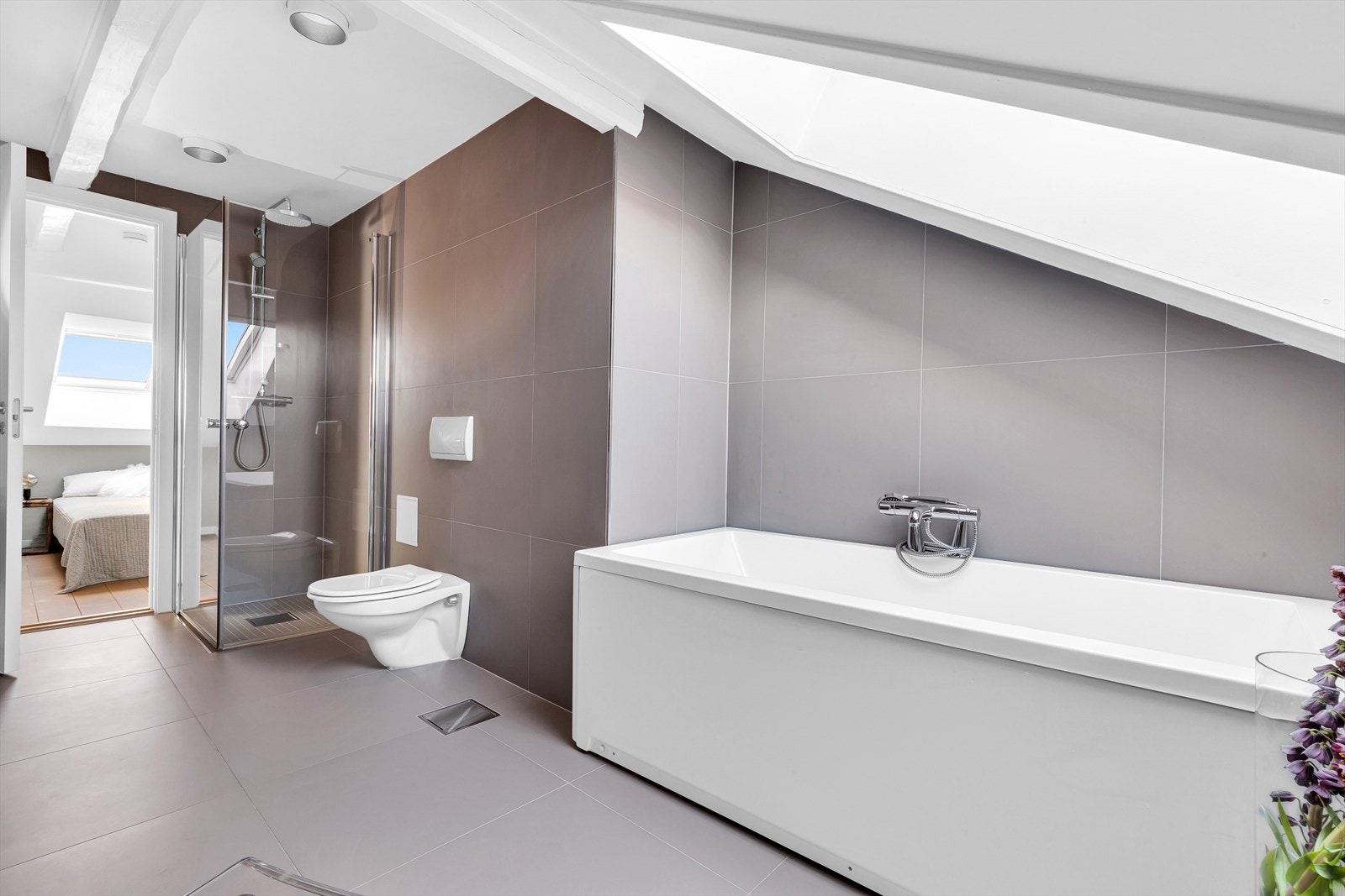 Badet er av god størrelse og har badekar med dusj, separat dusjnisje med innsvingbare glassdører, veggmontert wc og servant over pen og moderne innredning med skuffer. Galleribilde