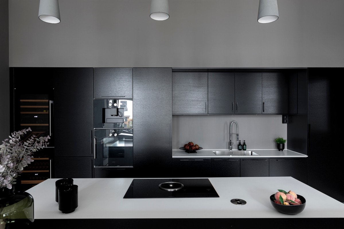 Kjøkkeninnredning med mørke, finerte fronter, Corian benkeplate og kum Galleribilde