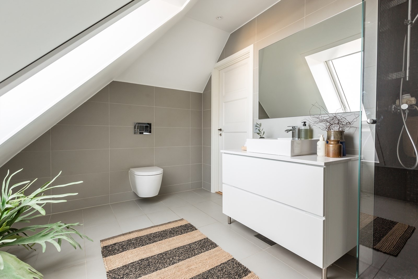 Badet i loftsetasjen er fra 2019 og fremstår som meget delikat med et tidløst design. Her er det valgt lekre, grå fliser på vegger og gulv. Galleribilde