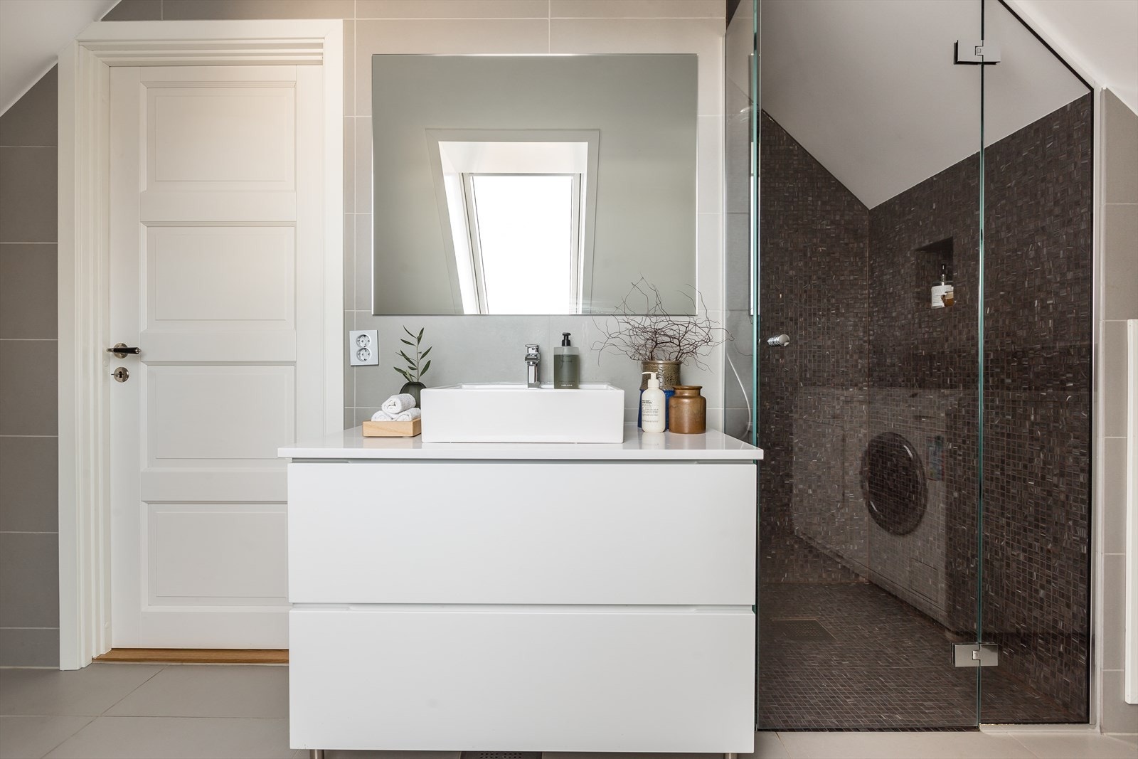 Mosaikkfliser i dusjnisjen. Badet har servant over skuffer, speil på vegg og vegghengt toalett. Galleribilde