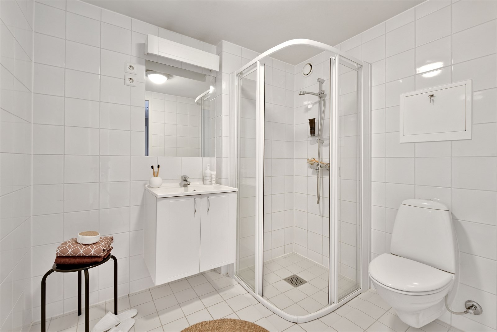 Badet har velholdte fliser i lyse fargetoner, med varme i gulv. Rommet er innredet med speil, belysning, servantseksjon, vegghengt toalett og en dusjnisje med skyvedør. Det er også opplegg for vaskemaskin. Galleribilde