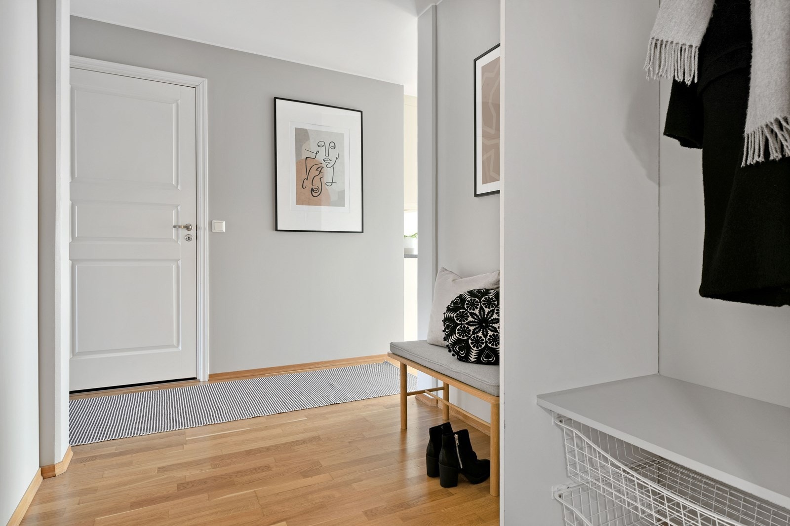 Entreen er pent innredet med eikeparkett på gulv, til grå vegger, i tråd med øvrige oppholdsrom. Det er ellers åpen garderobeløsning bestående av blant annet kurver og klesoppheng. Galleribilde