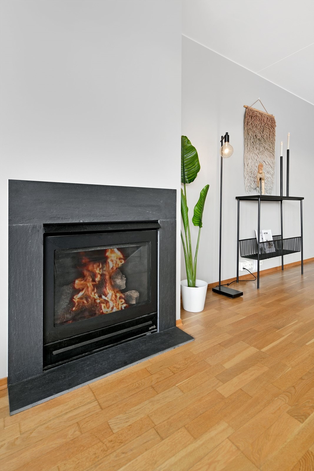 En gasspeis bidrar til både hygge og varme. Stuegulvet har eikeparkett og veggene er malt lysegrå. Galleribilde