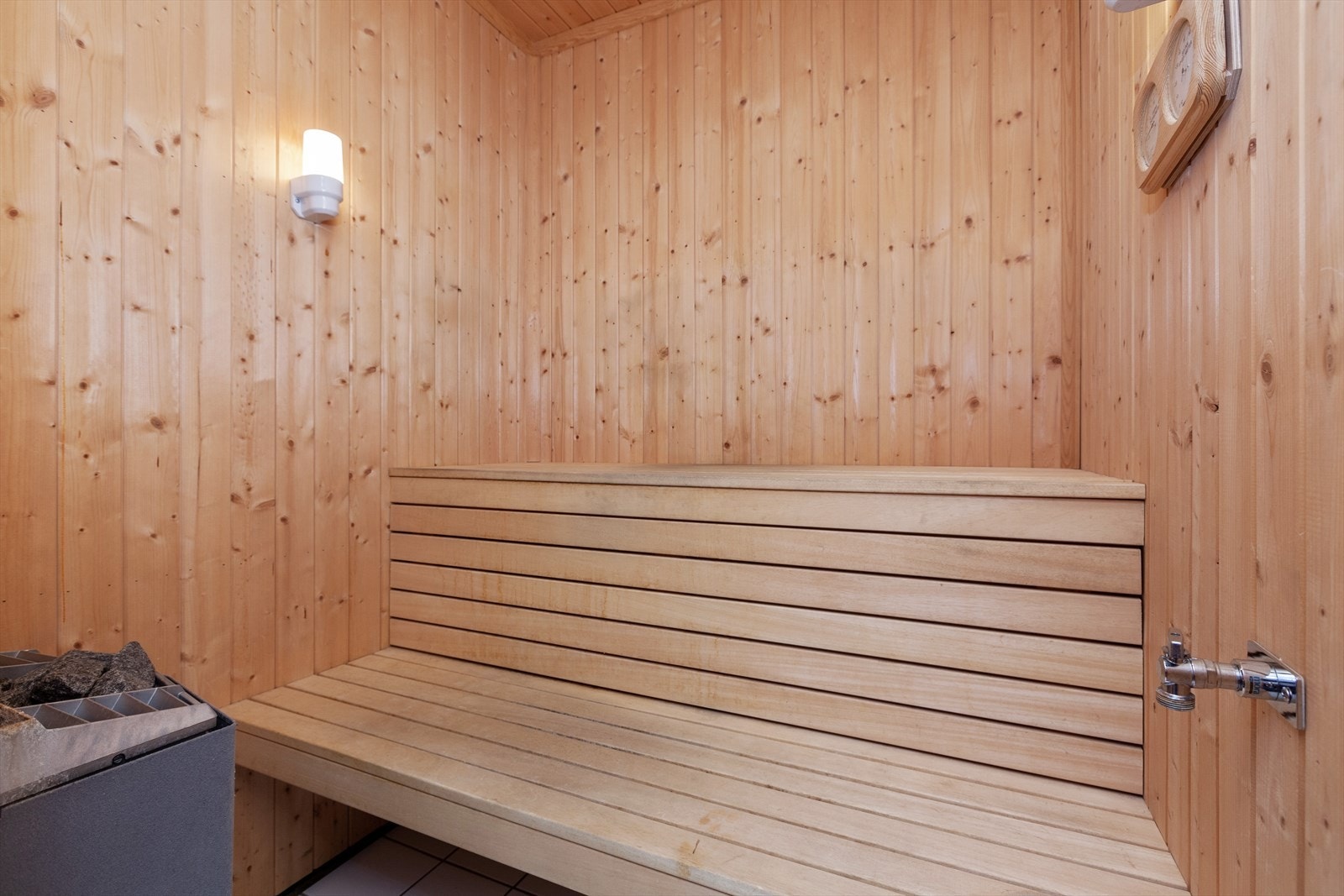 Badstuen har en sittebenk i tre, flislagt gulv og elektrisk badstuovn. Galleribilde