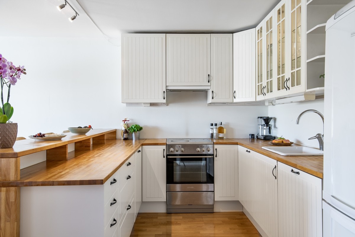 Kjøkkeninnredning fra Ikea med profilerte/glass fronter, Heltre benkeplate med enkel oppvaskkum med ett greps blandebatteri. Lys under overskap og i glasskap, ventilator med kullfilter. Galleribilde