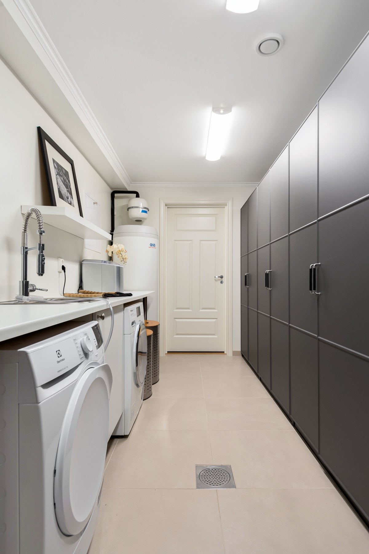 Boligens velutstyrte vaskerom ligger i kjelleren. Her er det lysmalte vegger og store, sandfargede gulvfliser over gulvvarme. Under benken er det et benkeskap i hvit, glatt utførelse, samt opplegg for både vaskemaskin og tørketrommel. Galleribilde