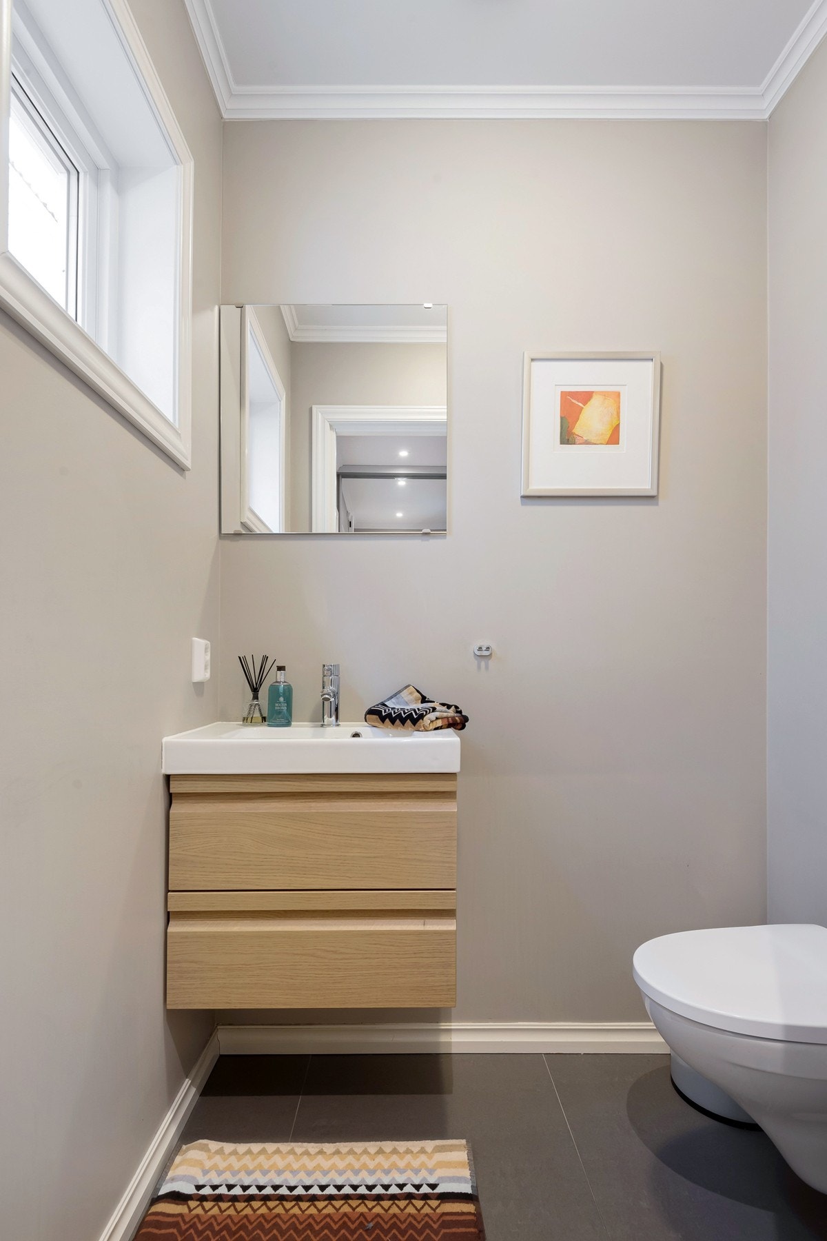 Gjestetoalettet er praktisk plassert i forbindelse med entreen i første etasje. Også her er det malte vegger og store gulvfliser med den samme, delikate fargepaletten som på badene. Himling er lyssatt med downlights og det er behagelig varme i gulvet. Galleribilde