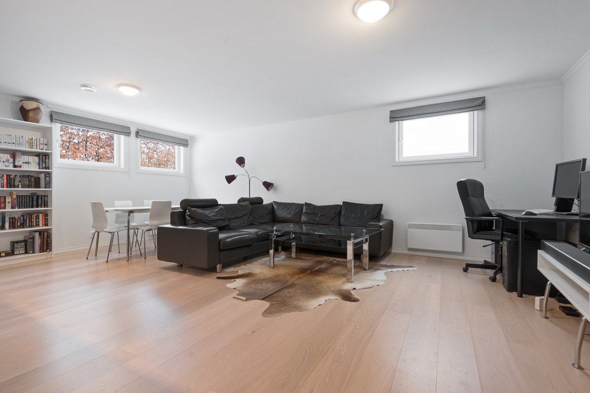 Stuen er holdt i en nøytral stil med enstavs eikeparkett og hvitmalte vegger. Videre er det lydhimling og tre høytsittende vinduer som bidrar med herlig dagslys. Rommets utforming gir god plass til både sofa, spisebord, tv-løsning og et arbeidsbord. Galleribilde