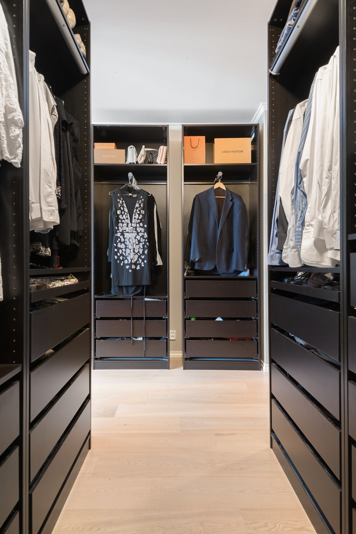 Omkledningsrom som er riktig godt utstyrt med fast belysning, hyller, skuffer og stenger i mørke skapstammer. Galleribilde