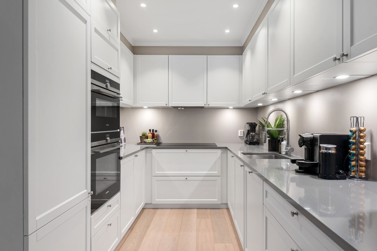 Kjøkkenet har takoppforede skap med profilerte hvite fronter i fin kombinasjon med en lekker Silestone benkeplate i grått. Integrerte hvitevarer er fra Siemens og består av en 90 cm bred induksjonstopp, stekeovn, dampovn, oppvaskmaskin og kjøl/frys. Galleribilde