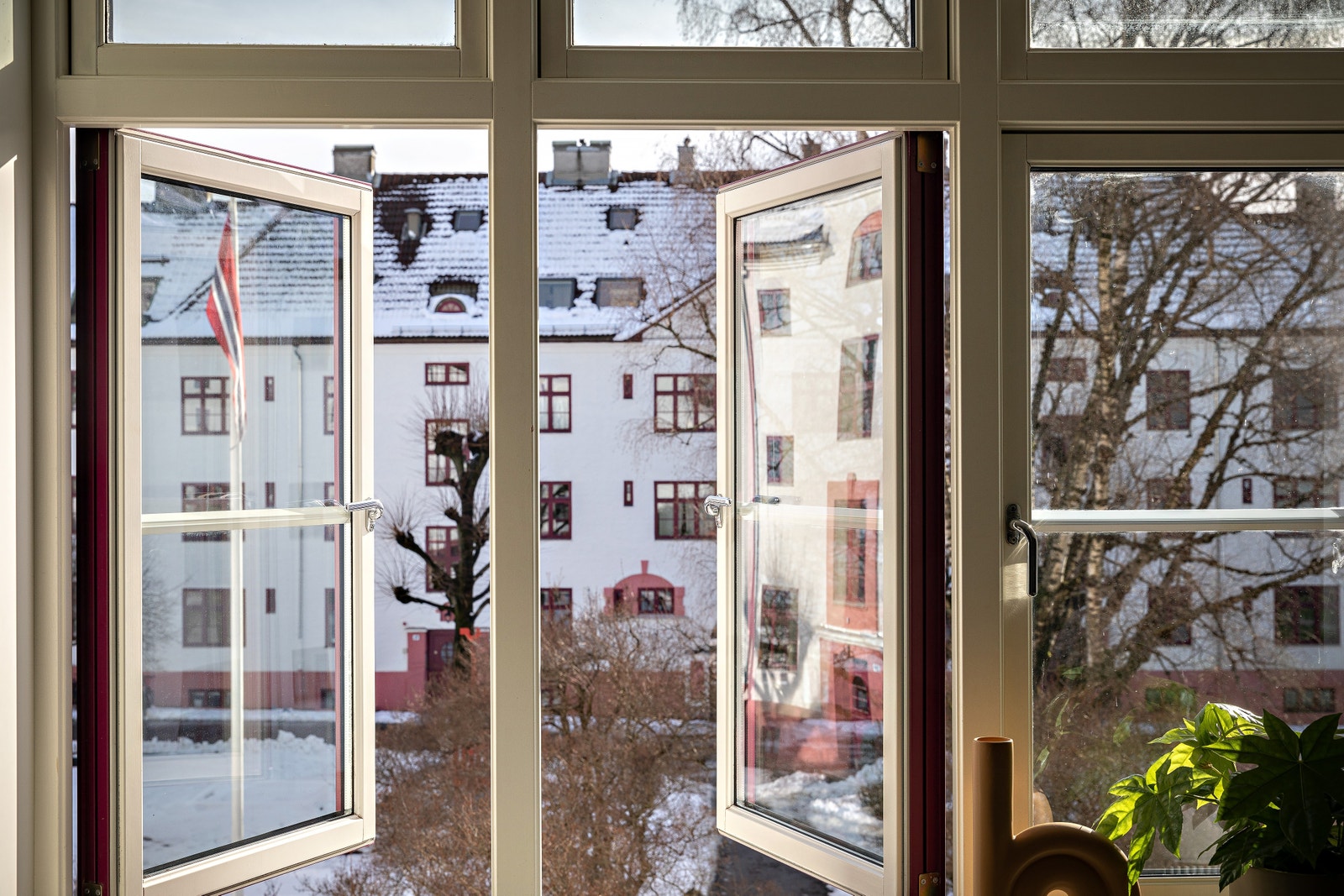 Stort stuevindu mot pent opparbeidet indre gårdsrom med beplantning, sykkelparkering, lekestativ og sittegrupper for sosiale sammenkomster. Galleribilde