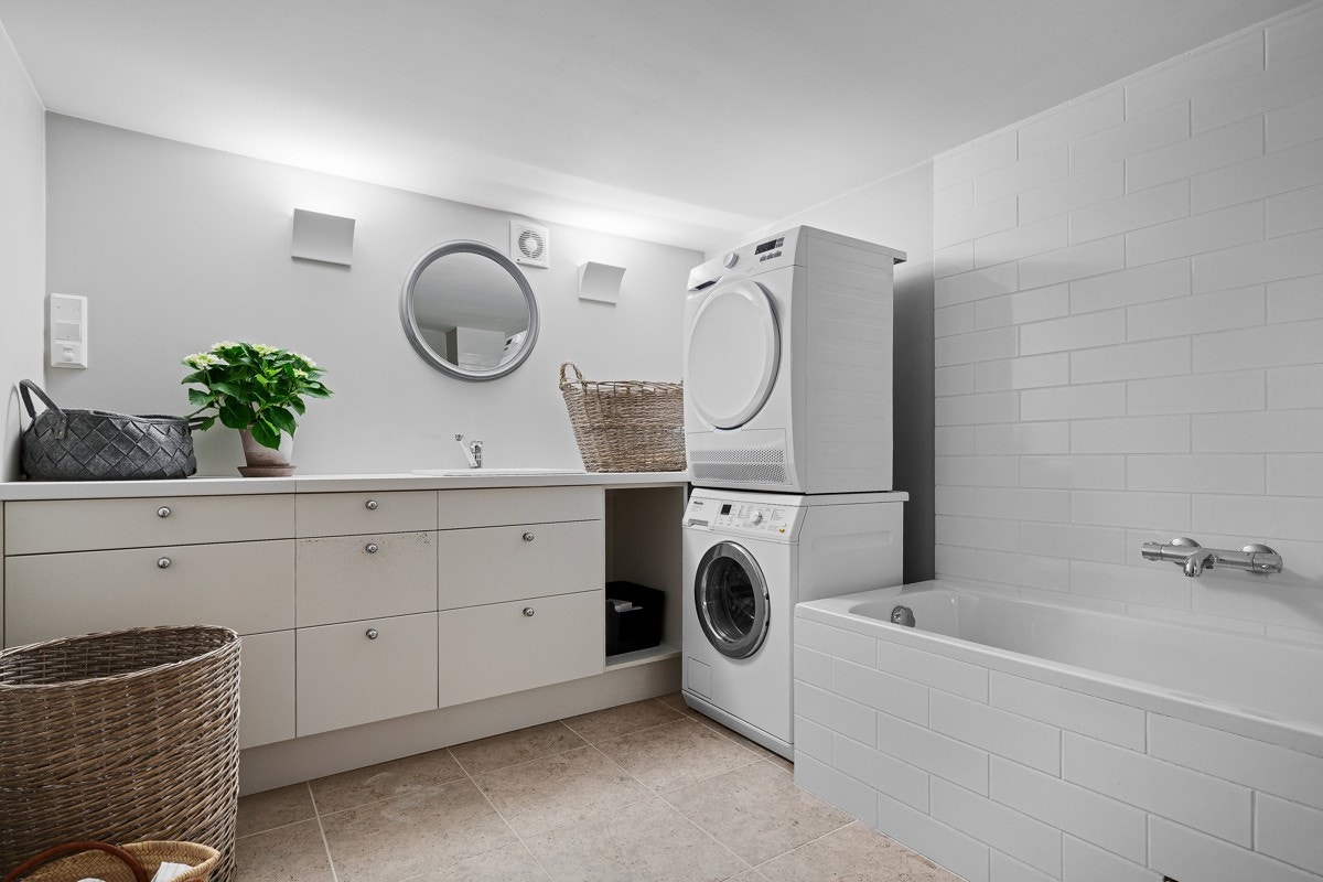 Romslig vaskerom med innfliset badekar og opplegg for vaskemaskin og tørketrommel Galleribilde