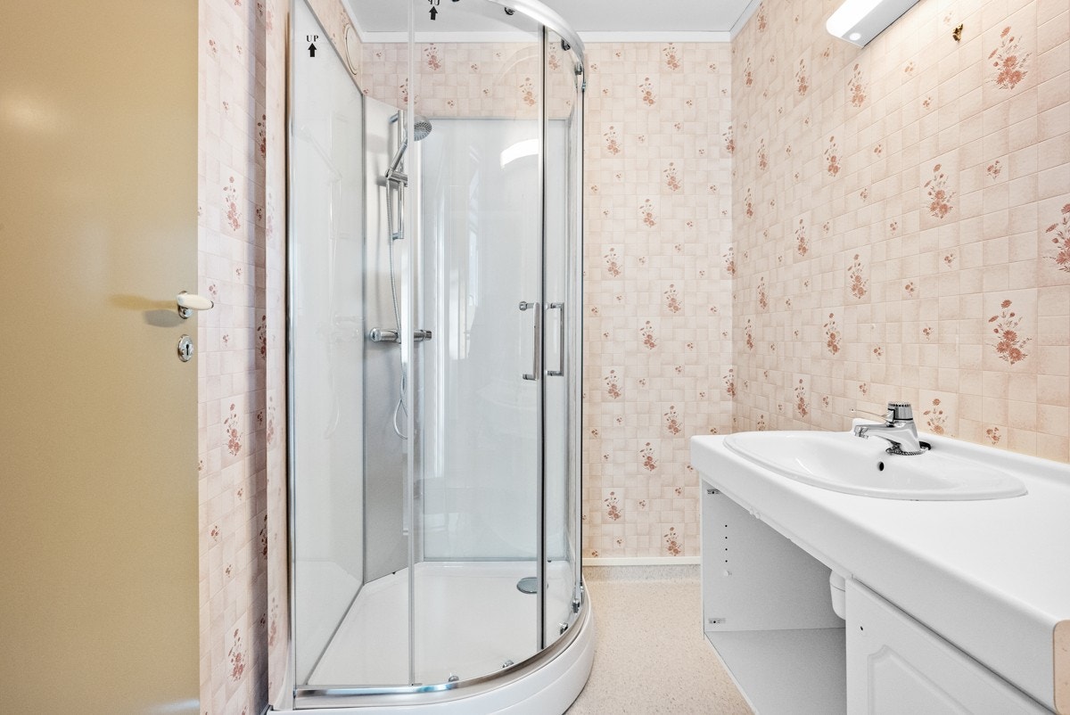 I gangen i 1. etasje finner man boligens bad. Badet fremgår fra byggeår og har enkel standard med våtromsbelegg og -tapet på gulv og vegger. Badet er i dag innredet med servant med underskap, vegglampe og dusjkabinett. Galleribilde