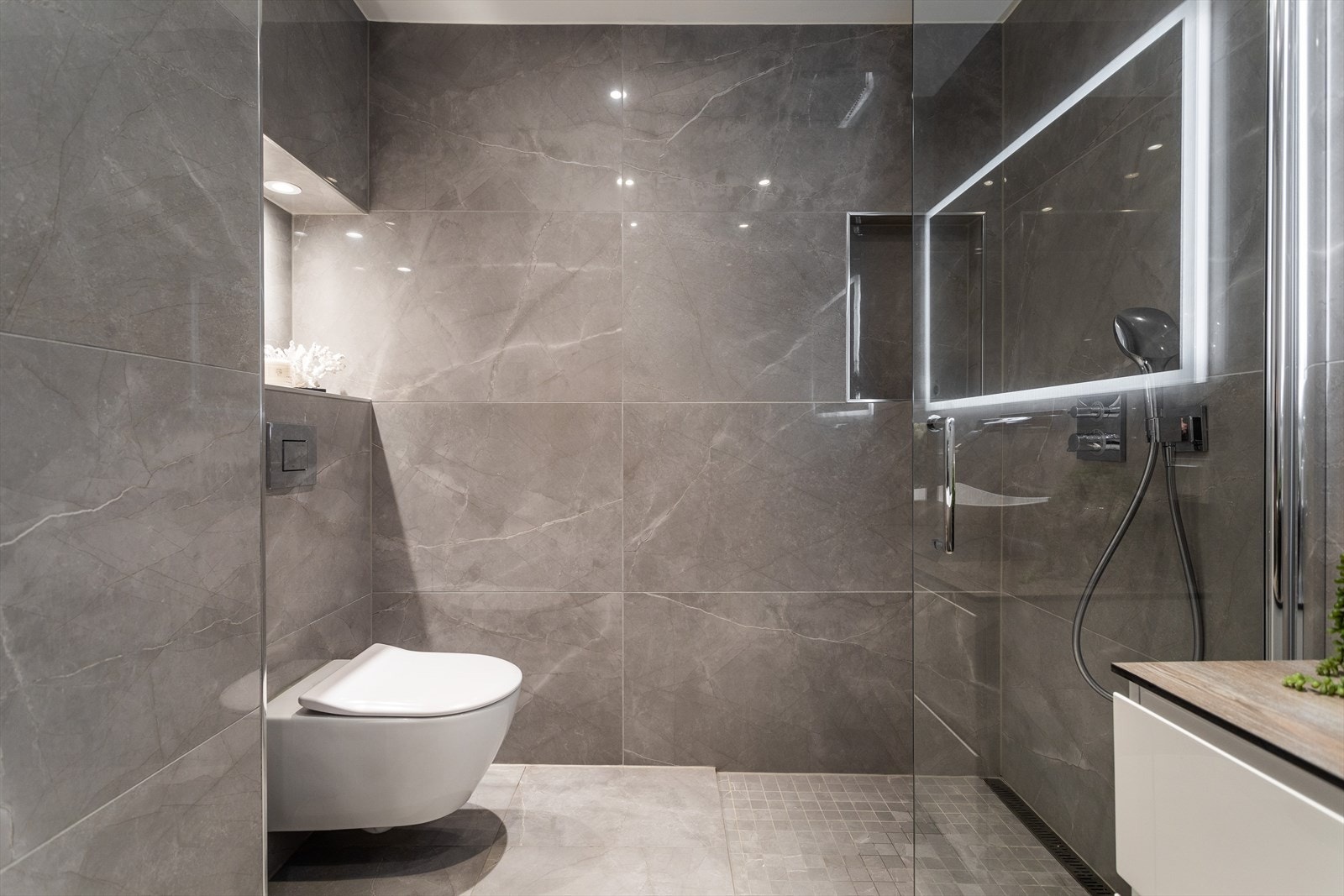 Dusjhjørne med glassvegg, integrert regndusj i himling, samt integrert dusjarmatur fra Hansgrohe. Vegghengt toalett fra Villeroy & Boch Galleribilde