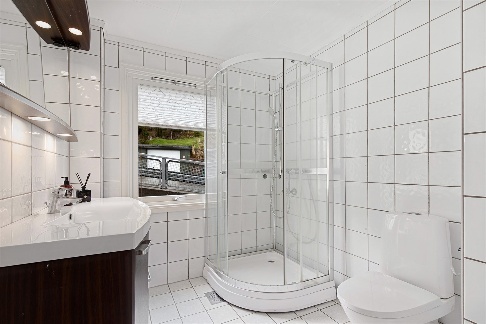 Pent flislagt bad innredet med servant nedfelt i innredning med speil og lys over, dusjkabinett samt toalett. Galleribilde