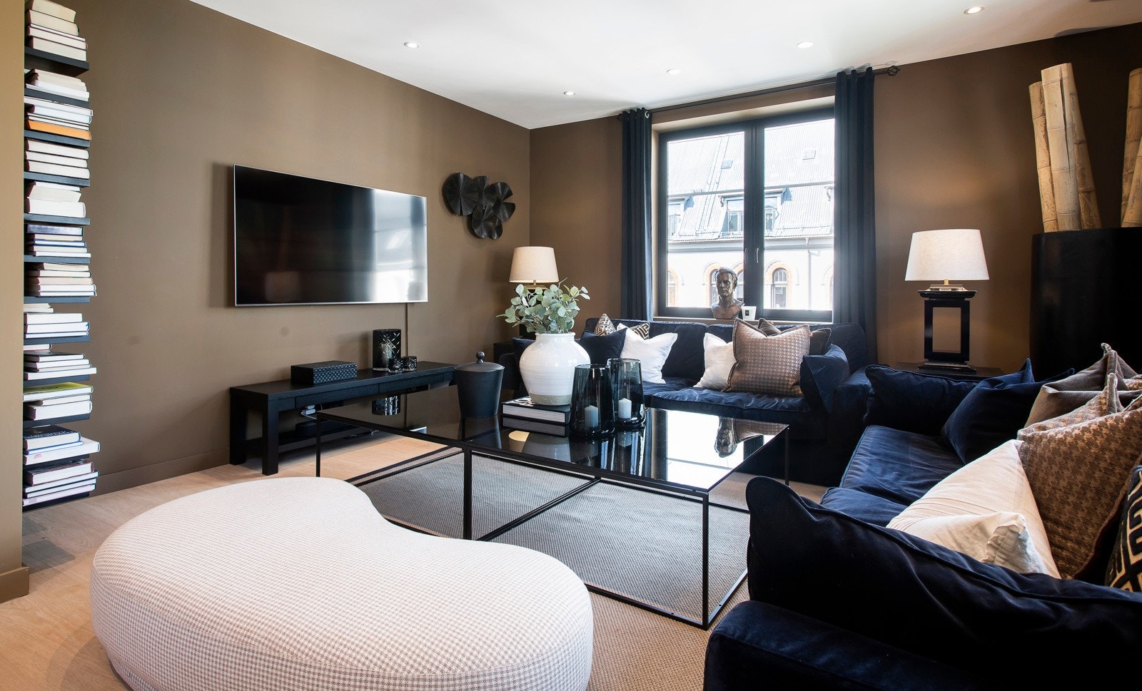 Store vinduer slipper inn godt med dagslys til stuene, og det naturlige lyset suppleres ypperlig av downlights i store deler av himlingene. I den ene stuen er det montert en stilren bokhylle i sort, og det er god plass til en stor sofagruppe. Galleribilde