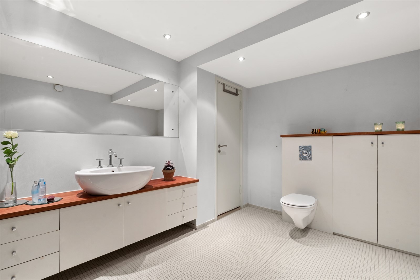 Utstyrt med åpent dusjhjørne med termostatbatteri, innmurt badekar, veggmontert toalett, helstøpt servant og servantskap. Galleribilde