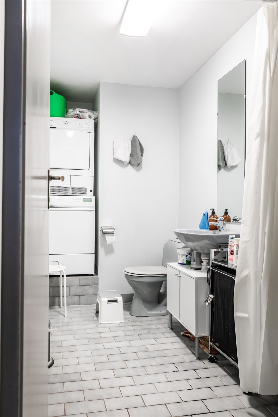 Badegulv med fliser og gulvvarme, veggflater med malte flater og fliser. Videre har badet åpen dusjplass, gulvmontert toalett, helstøpt servant med ett-greps bl.batteri og servantskap. Opplegg for vaskemaskin. Galleribilde