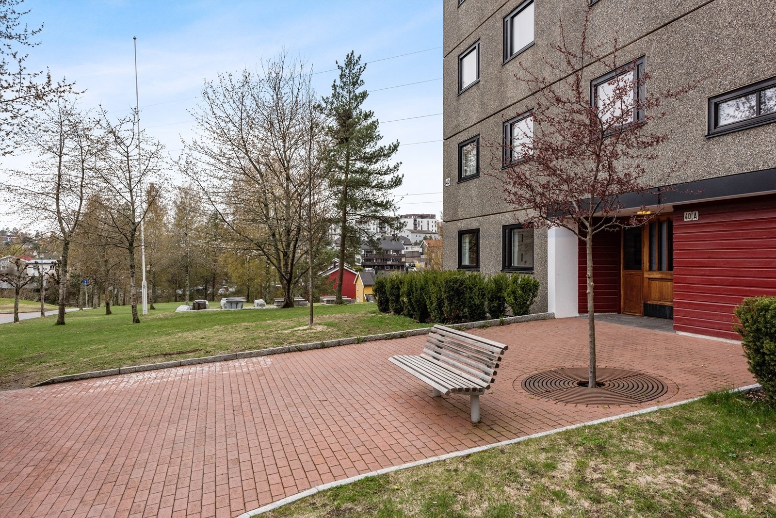 Pent opparbeidet fellesareal med gressplen, prydbusker, hekker, trær, sykkelstativ, lekeapparater, benker, bord og asfalterte gangveier. Galleribilde