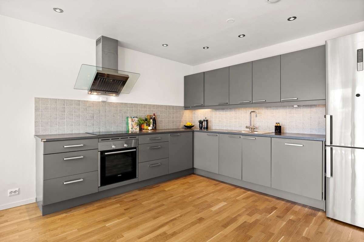 Huseby kjøkkeninnredning med grå glatte fronter og grå laminert benkeplate. Røroshetta avtrekksventilator over kokesone med direkte utlufting. Galleribilde