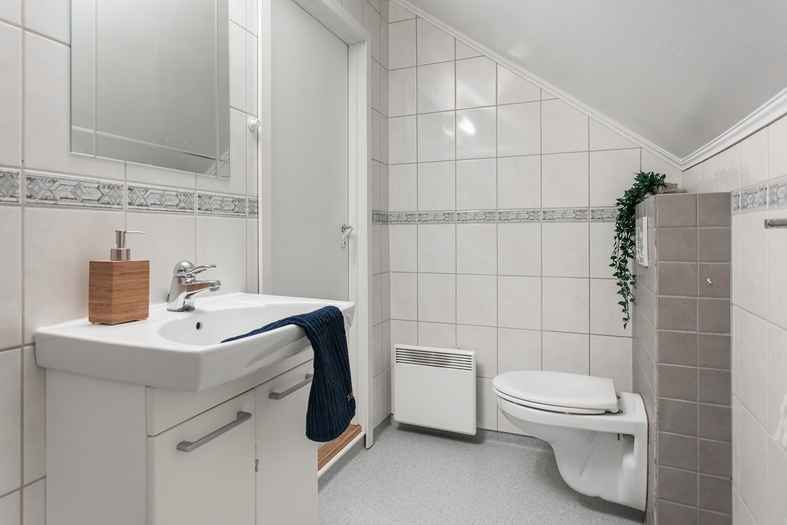 Badet er holdt i lyse farger med flis på vegger. Veggmontert toalett og åpen dusj Galleribilde