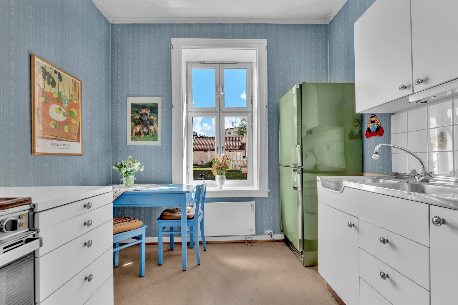 Fliser mellom benkeskap og overskap. samt benkeskapsbelysning og stikkontakter under overskap. Frittstående hvitevarer som kKjøleskap med frysedel og komfyr Galleribilde