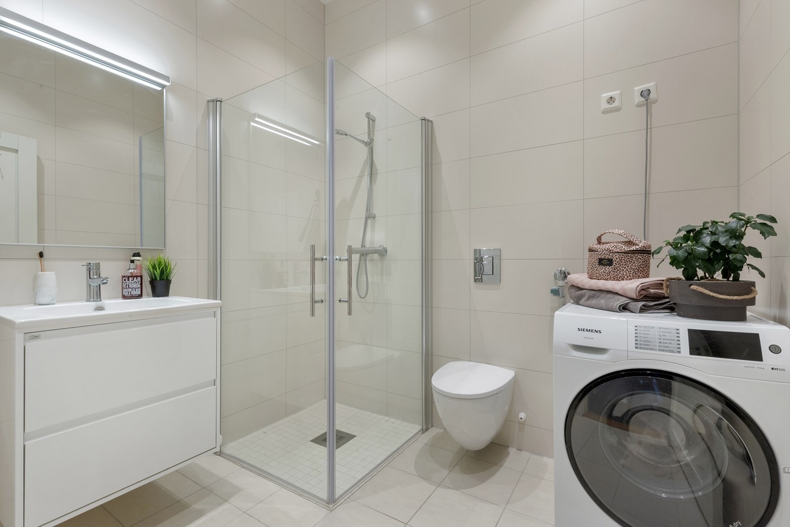 Leiligheten har et romslig og lekkert bad med flissatte overflater, moderne innredning og opplegg for vaskemaskin og tørketrommel. Galleribilde