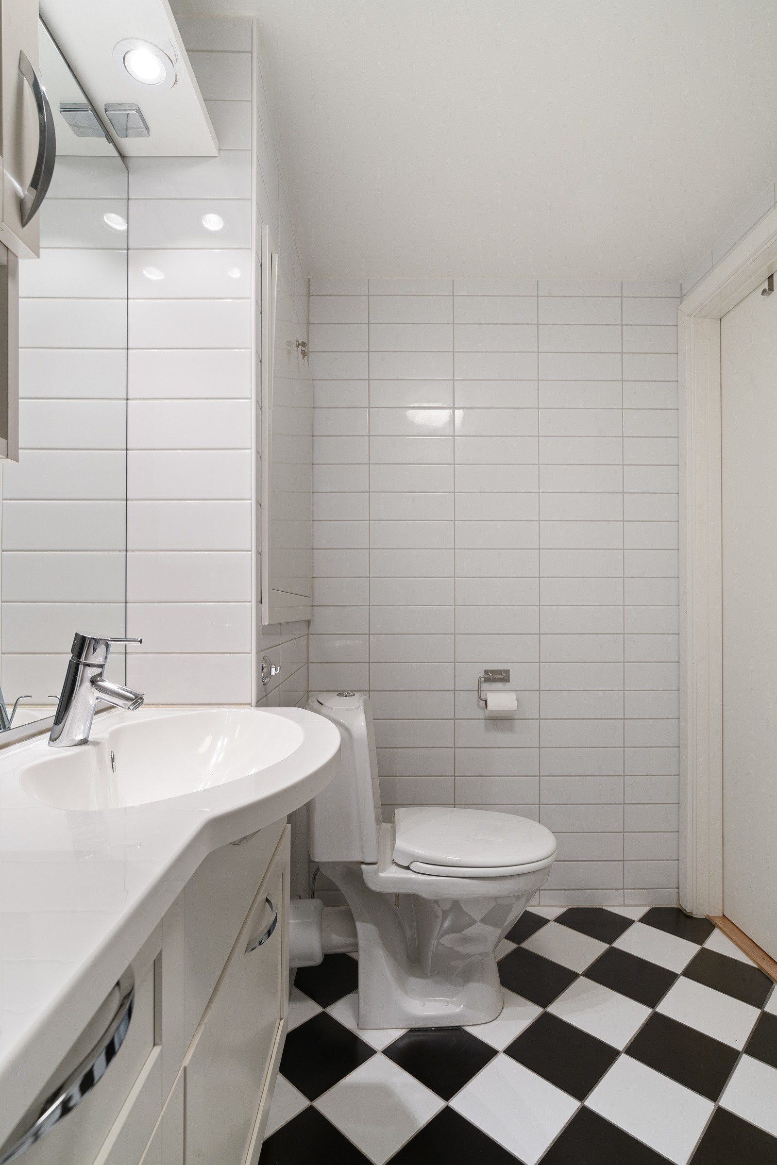 Badet er innredet med gulvmontert toalett, servant med underskap, dusjhjørne med glassdører og opplegg for vaskemaskin