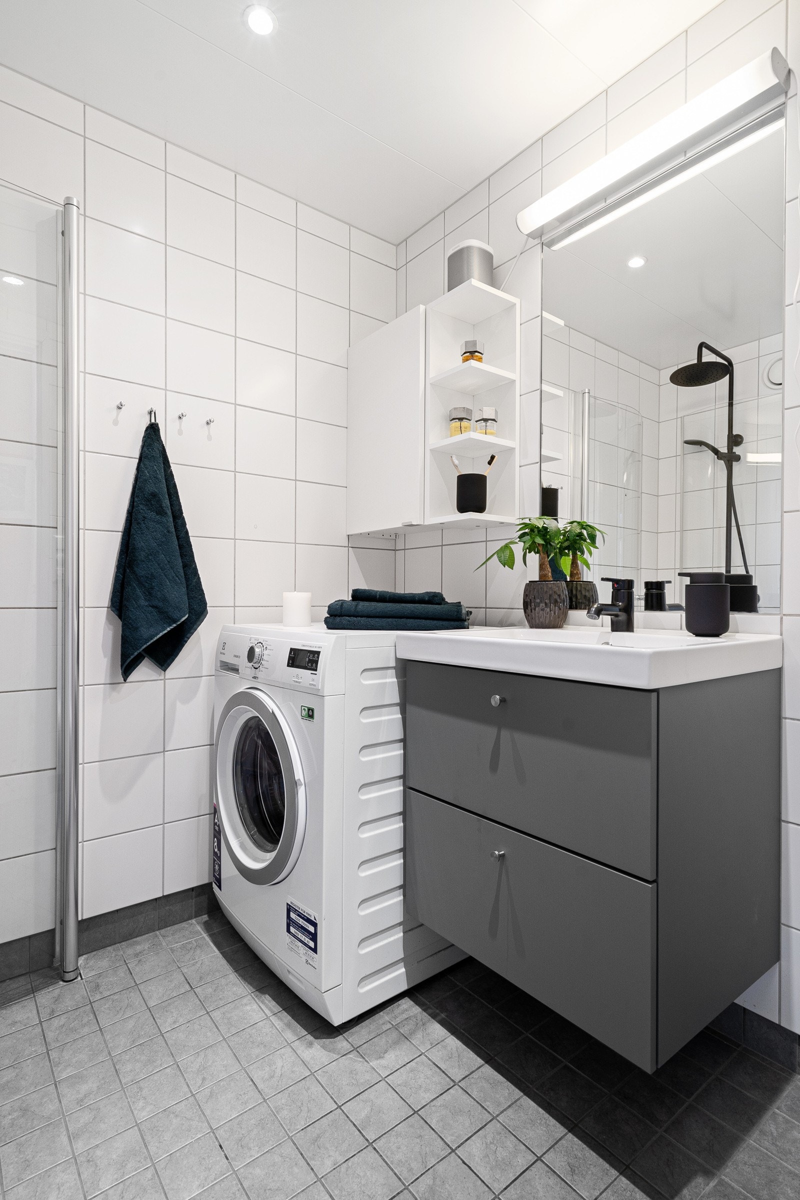 Servant med skuffer i innredning under, samt speil med belysning over. Opplegg for vaskemaskin i hjørnet, samt veggskap over. Galleribilde