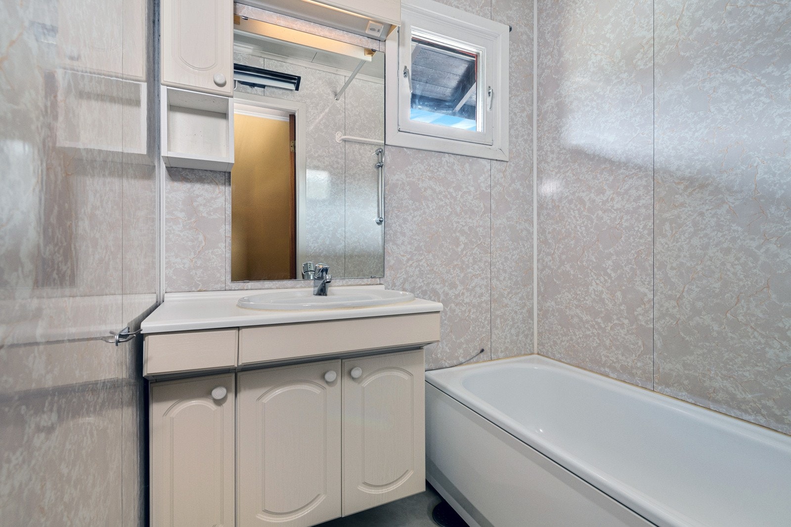 Badet er holdt i lyse toner med vinyl på gulv og våtromspanel på vegger. Badet har stråleovn, innsynsfritt vindu og et badekar med dusjarmatur. Galleribilde