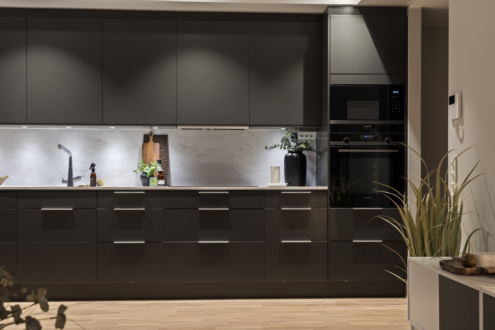 Integrerte hvitevarer som oppvaskmaskin, mikrobølgeovn, stekeovn med pyrolyse og induksjon koketopp med ekstra stor kokeplate og ventilator over samt "side-by-side" kjøleskap i nisje Galleribilde