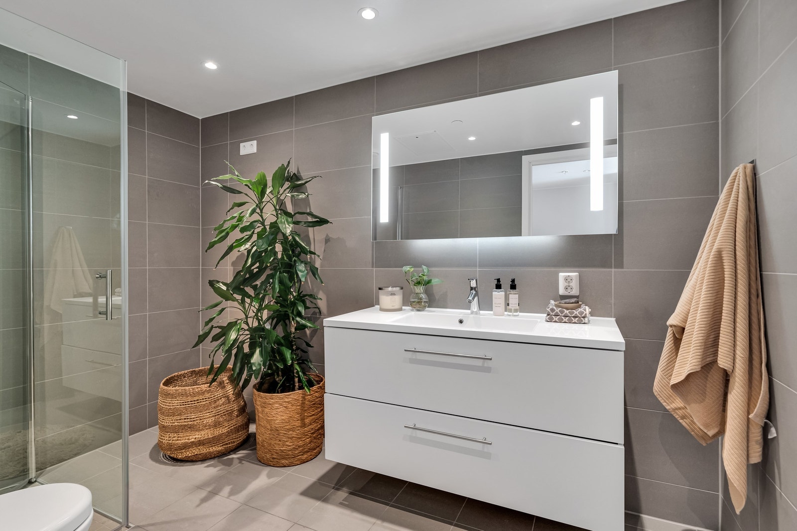 Delikat baderom med grå fliser på gulv og vegger, varme i gulv og downlights i tak Galleribilde