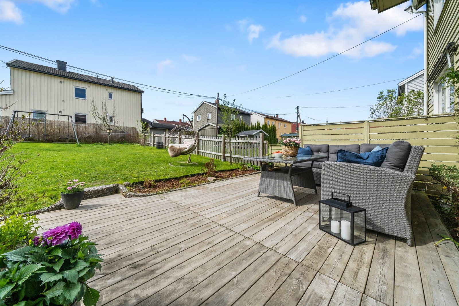 Uteplass på flere sider av boligen hvor den ene er opparbeidet med terrasseplatting og en hage som er beplantet med trær, busker og hekk Galleribilde