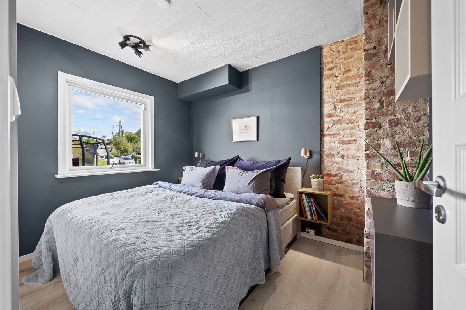 Hovedsoverommet er malt i en mørk, avslappende fargetone, og det er en stilig kontrastvegg kledd i rød teglstein Galleribilde