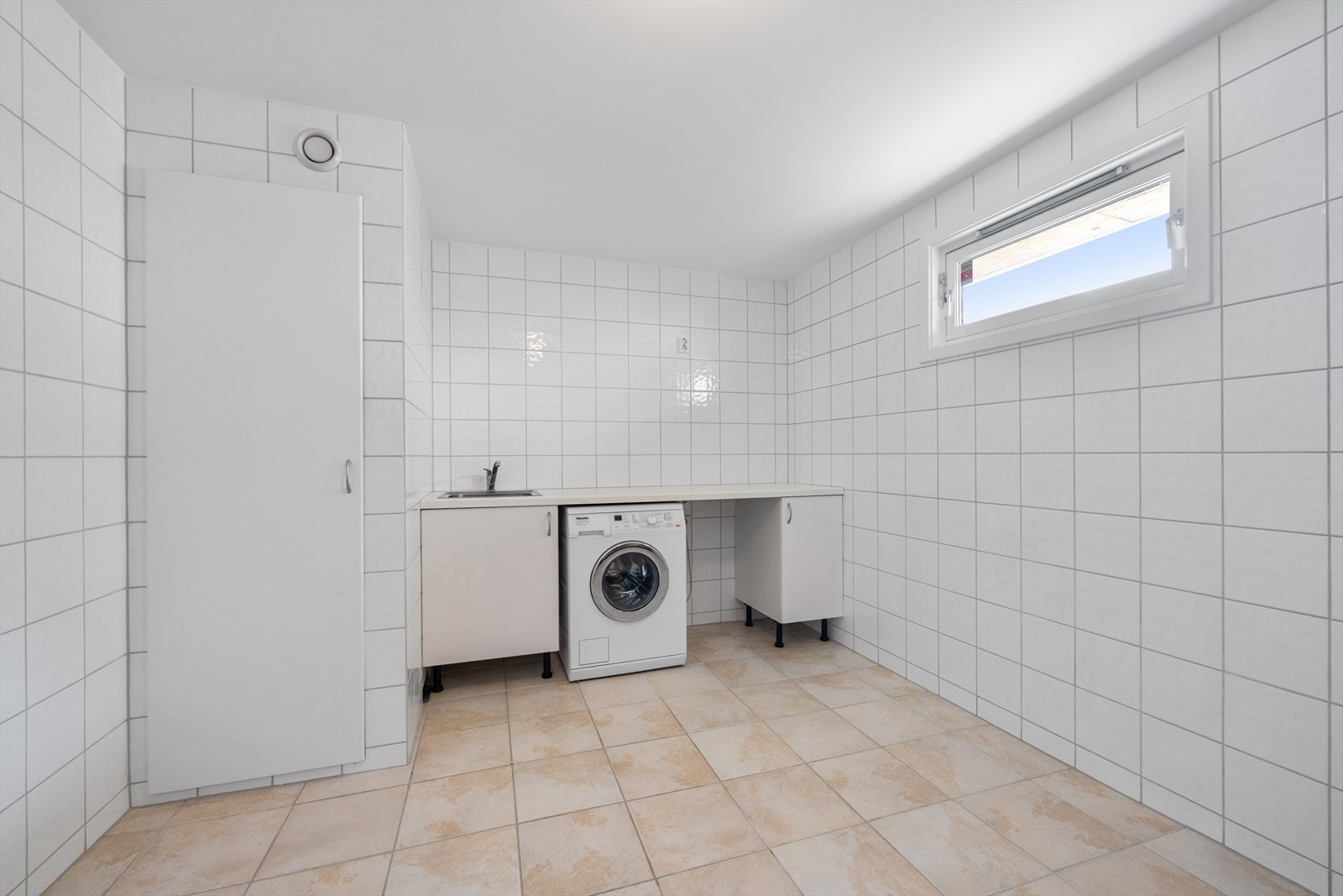 Stort og praktisk vaskerom med enkel innredning med oppvaskbenkeskap og benkeplate med nedfelt oppvaskkum med blandebatteri. Det er opplegg for vaskemaskin. Galleribilde