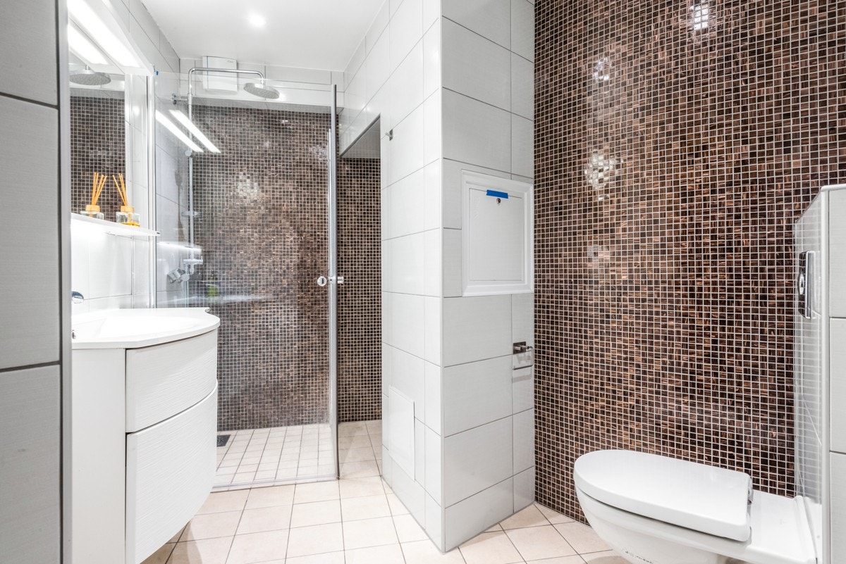 Badet ved hallen er innredet med servantskap, opplegg for vaskemaskin og stor dusjnisje med tropisk regn og hånddusj. Galleribilde