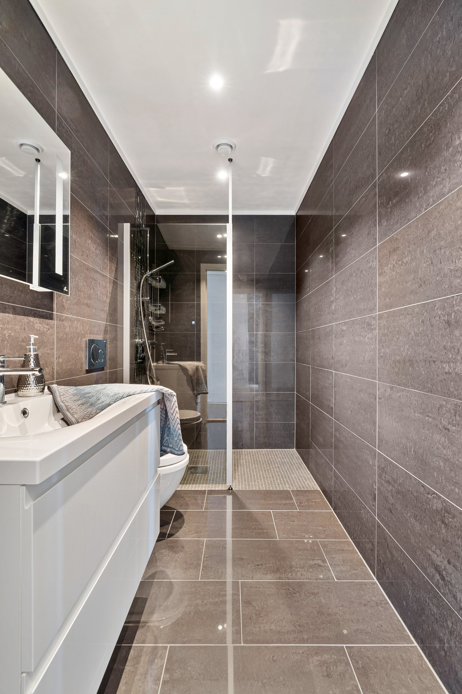 Badet er innredet med vegghengt toalett, dusjnisje med fast glassvegg samt servant med speil og underskap