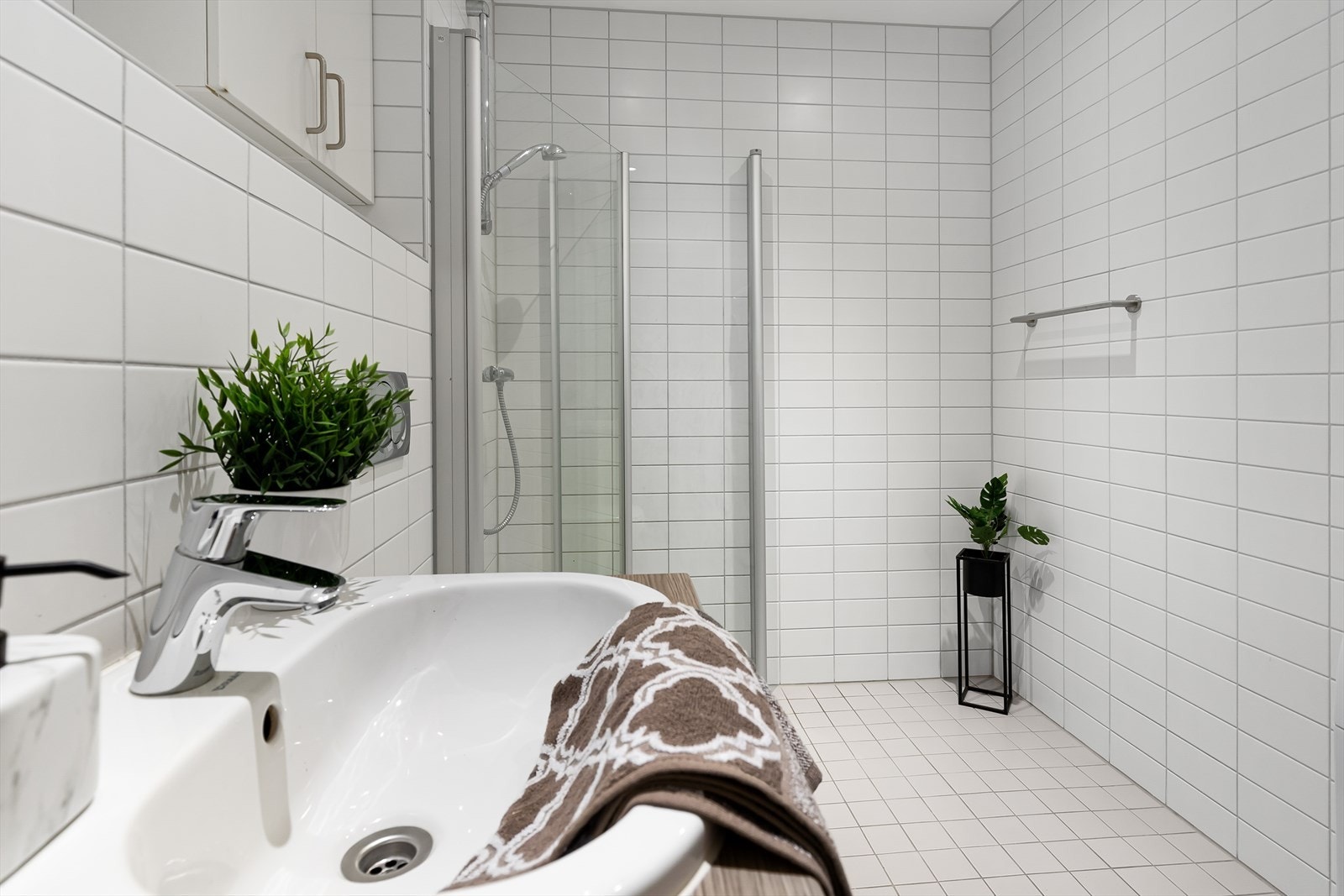 Baderommet med adkomst fra gang har dusjhjørne med dører i herdet glass. Benkeplate med nedfelt servant. Veggskap. Vegghengt toalett. Galleribilde