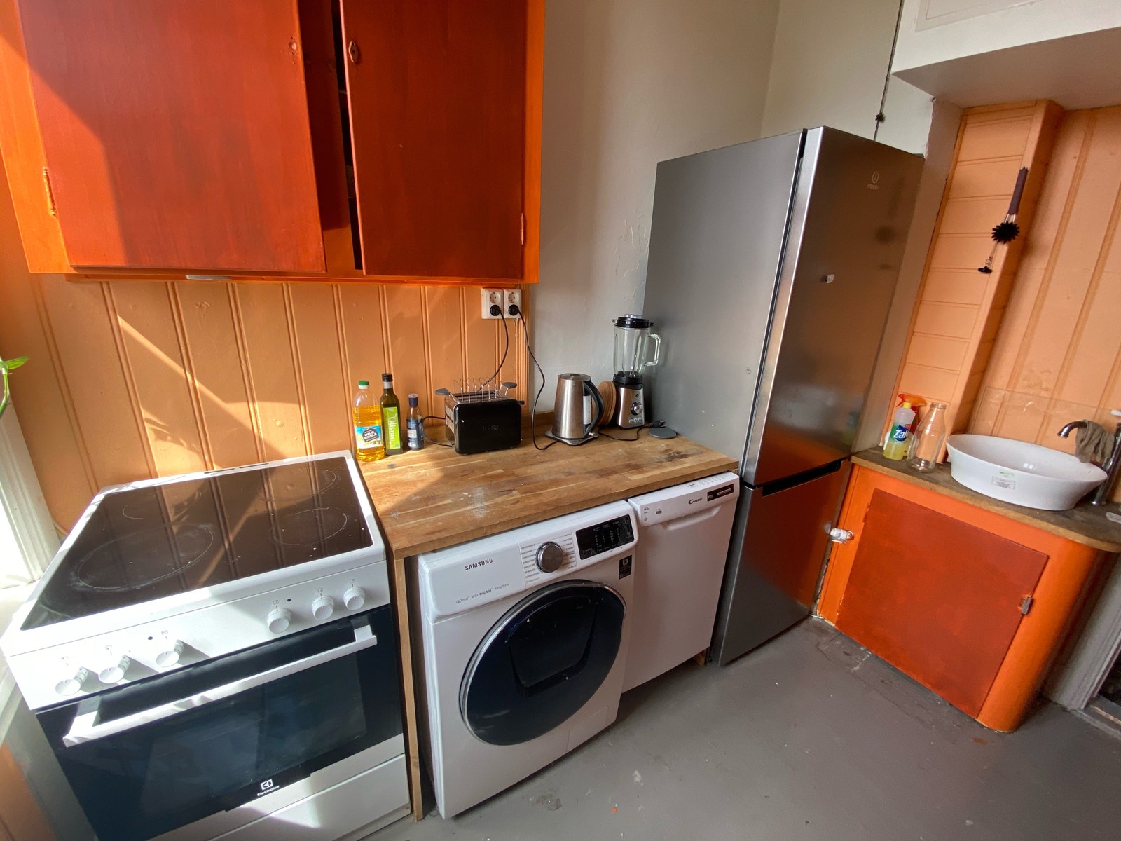 kjøkken innredet med kjøleskap/frys, oppvaskmaskin, vaskemaskin og tørketrommel i ett, og komfyr Galleribilde