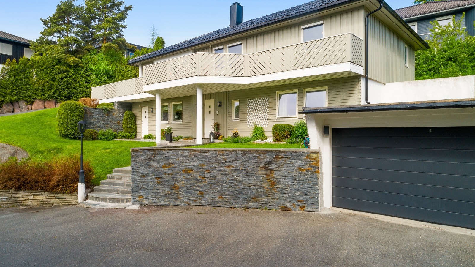 Fra en stor, asfaltert gårdsplass er det støpt mur med skiferforblending, samt en støpt trapp med skifer opp til inngangspartiet. Galleribilde