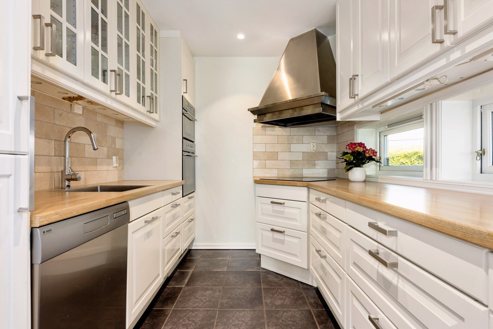 Kjøkkeninnredningen har integrerte hvitevarer som platetopp (induksjon), stekeovn, mikrobølgeovn, vinskap og kjøleskap Galleribilde